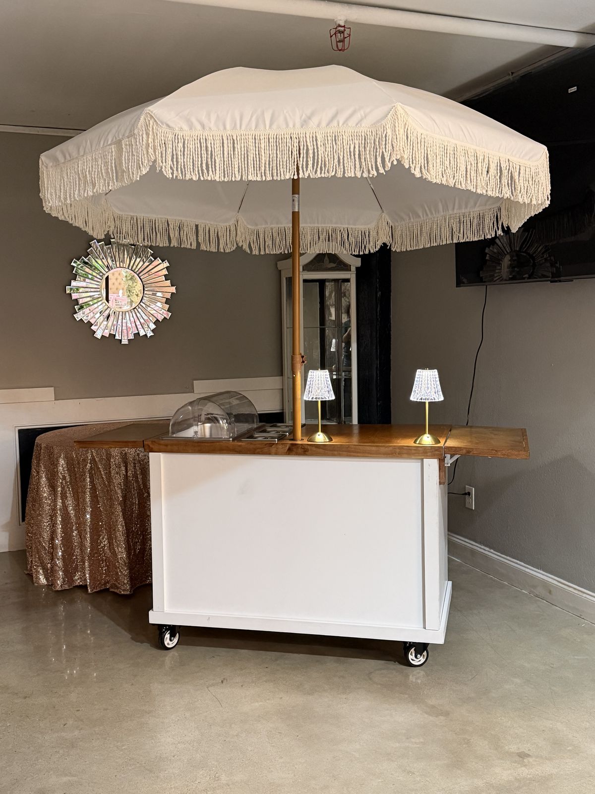 The snack cart, white with a wood top and a fringed white umbrella